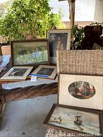Six framed vintage artworks arranged on wooden table including landscapes and portraits