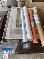 Posters, some rolled in tubes, others flat, largest size approximately 36x24 inches visible under plastic wrap.