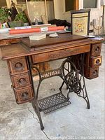 Antique Singer sewing machine table with carved wooden drawers and cast iron treadle base outdoors.