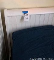 Close shot of white wooden headboard with label showing condition/tag attached. Panel design visible.