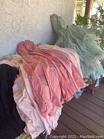 Pile of pastel taffeta and tulle dresses in pink, ivory and green stacked on a porch floor