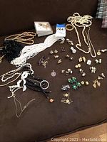 Lot of costume jewelry spread on brown surface showing pearl necklaces, seed pearl necklaces, black bead necklaces, and numerous clip-on earrings with various designs.