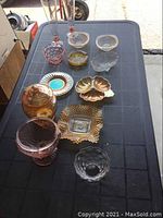Overview of 13 mixed vintage glass pieces on black table, showing various shapes and colors including amber, pink, clear and blue-green glass.