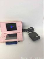 Pink Nintendo DS Lite handheld gaming console powered on with charger next to it, showing Game Freak logo screen.