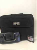 Black carrying case with SEGA Game Gear logo, black Sega Game Gear handheld console, and one game cartridge.