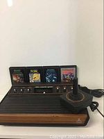 Atari 2600 console with joystick controller and four game cartridges lined up behind it.