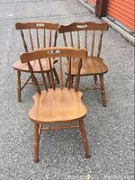 Three wooden chairs grouped outdoors on pavement showing front and back views.