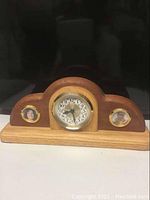 Front view of the wooden mantel clock showing two small circular photo holders with photos inside on each side of the clock face.