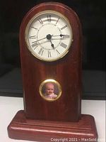 Front view of the wooden clock with white dial, black Roman numerals, gold rim, and circular photo holder with baby's picture.