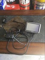 TomTom GPS device with associated cables including car charger and power adapter laid out on a stone surface.