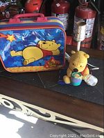 Winnie the Pooh lamp next to lunchbox on a surface with fire extinguishers in the background