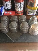 Seven antique glass insulators placed together on a dark slate surface with fire extinguishers in the background, showing forms and relative size.