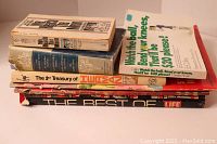 Stack of books and magazines including Paris Match, Reader's Digest, Treasury of Herman, Life book and an illustrated State Farm atlas.