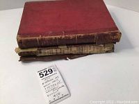 Three stacked vintage books including a red hardcover and two with worn spine and damaged covers.