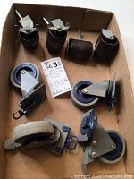 Photo showing four black rubber castors with threaded stems (two swivel, two fixed) and four blue/gray plastic wheels with metal mounting plates in cardboard box