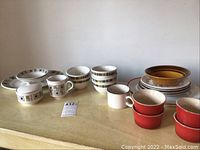 Photo shows the full lots of vintage dishes on a yellow tablecloth background including patterned bowls, creamers, and cups.