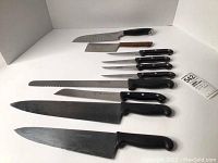 Photo showing all knives and cutting utensils laid out, including J.A. Henckels knives, steak knives, large cutting knives and cleaver.