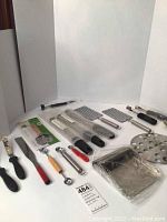 Photo showing all kitchen graters, scoops, melon ballers, corers, utensils and trivet arranged on a white surface.