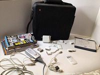 Photo showing black Apple Macintosh soft cover briefcase, eleven assorted magazines, various Apple adapters and cords spread around