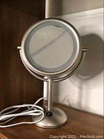 Front-facing view of the light up magnifying mirror showing round, dual-sided mirror with metallic stand, cord coiled beside base.