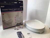 Raised toilet seat with lid in original packaging, including installation hardware and instruction manual.