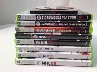 Stack of Xbox 360 game cases showing titles: Tiger Woods PGA Tour 07, Madden NFL 07 Hall of Fame Edition, Guitar Hero Legends of Rock, NHL 07, NHL 09, NHL 10.