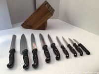 Set of 9 black-handled knives and a wooden knife block on a white surface