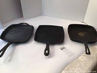 Three square cast iron skillets with ribbed surfaces on a white background