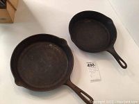 Photo of two round cast iron frying pans showing one larger and one smaller pan with handles and dual spouts.