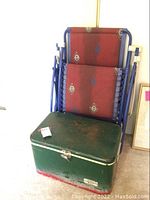 Vintage metal Thermos cooler stacked in front of blue frame anti-gravity chair with red decorative fabric.