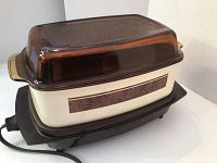Front-side view of vintage West Bend slow cooker with brown glass lid and cream body.