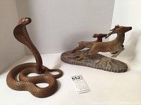 Front view of both wooden carved cobra and deer pair together on white background with lot number in front.