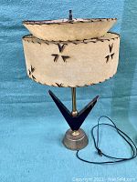 Full view of the lamp showing the double fibreglass shade with decorative cut-outs, attached to a geometric metal base.