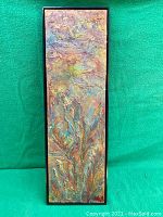 Front view of elongated rectangular textured abstract painting in colors of gold, copper, bronze, blue, and green featuring floral forms and signed by Ruth Maier in bottom right corner. Black frame included.
