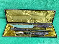Full view of antique carving set in lined case showing knife, fork, and sharpening steel with bone (antler) handles.