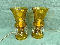 Front view of pair of amber glass mantle lustre lamps showing cut to clear star and diamond patterns, crystal prism dangles, and light bulbs installed.