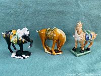 Three pottery horse figurines side-by-side on teal surface, showing overall condition and colors.