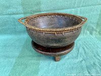 Side view of the dark wood bowl with detailed woven rim, resting on round wooden stand with three legs.