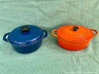 Two enameled cast iron cookware pieces, orange Le Creuset and blue enamelled pot.