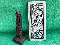 Wooden totem carving and Thunderbird plaque side by side on green background.