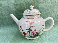 Front three-quarter view of globular white porcelain teapot with hand-painted famille rose floral and bamboo decoration