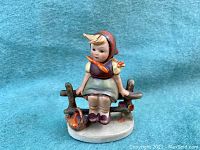 Front view of the figurine showing the young girl seated on the fence with a bird near her feet, hand-painted details and colors visible.