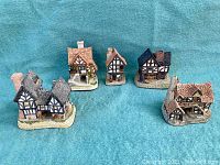 Five miniature Tudor-style houses arranged on blue fabric background showing different architectural styles and roof colors.