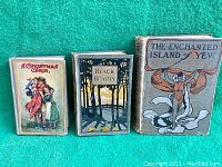 Three old books standing side by side on a green fabric background. From left to right: 'A Christmas Carol,' 'Black Beauty,' and 'The Enchanted Island of Yew'. Covers show wear and aging.