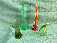 Photo showing all four blown glass items on a grayish fabric backdrop: the tall green ruffled vase, the smaller dark green ruffled vase, the red and clear swirl vase, and the light green handled pitcher.