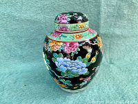 Front right diagonal view of the antique oriental ginger jar showing its black base with colorful floral patterns and matching lid.