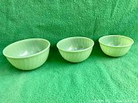 Set of three vintage Fire King jadeite mixing bowls of graduated sizes displayed on green background.