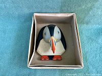 Top view of the puffin-shaped wooden door knocker in a box showing detailed paint and shape.