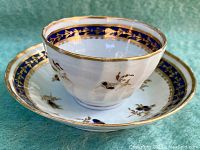 Side view of tea bowl on saucer showing blue and gold floral decoration and octagonal shape.