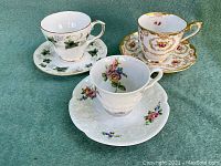 Three vintage porcelain tea cups each with a matching saucer, different floral and foliage patterns with gold trim.